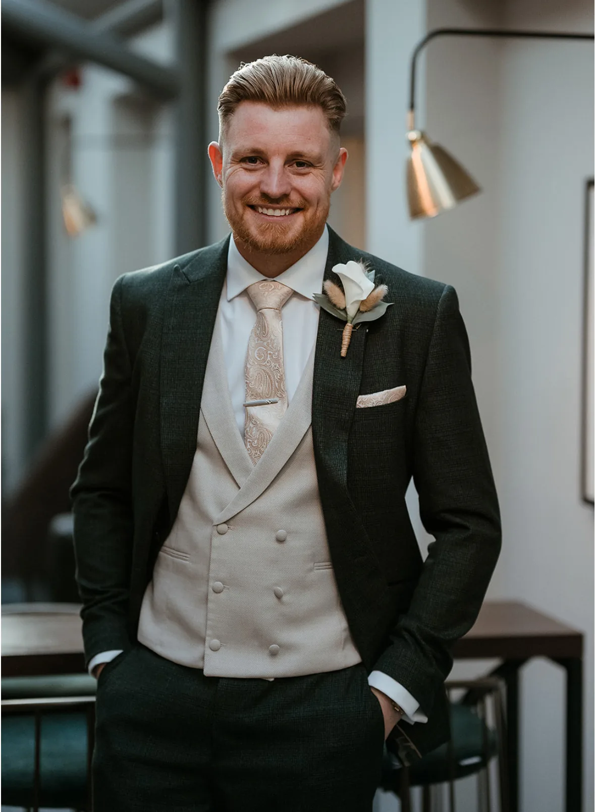 Groom in a dark green three piece suit with a cream double breasted waistcoat, paisley tie and rose buttonhole