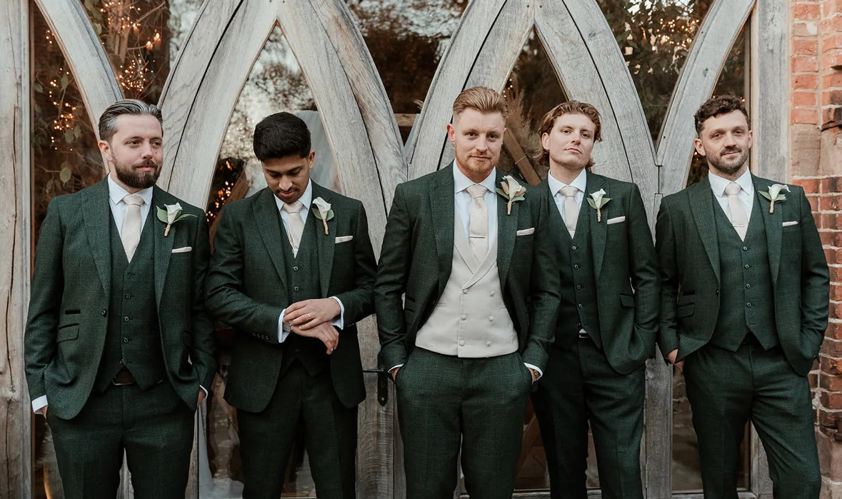 Groomsmen in green three piece suits with cream ties and rose buttonholes