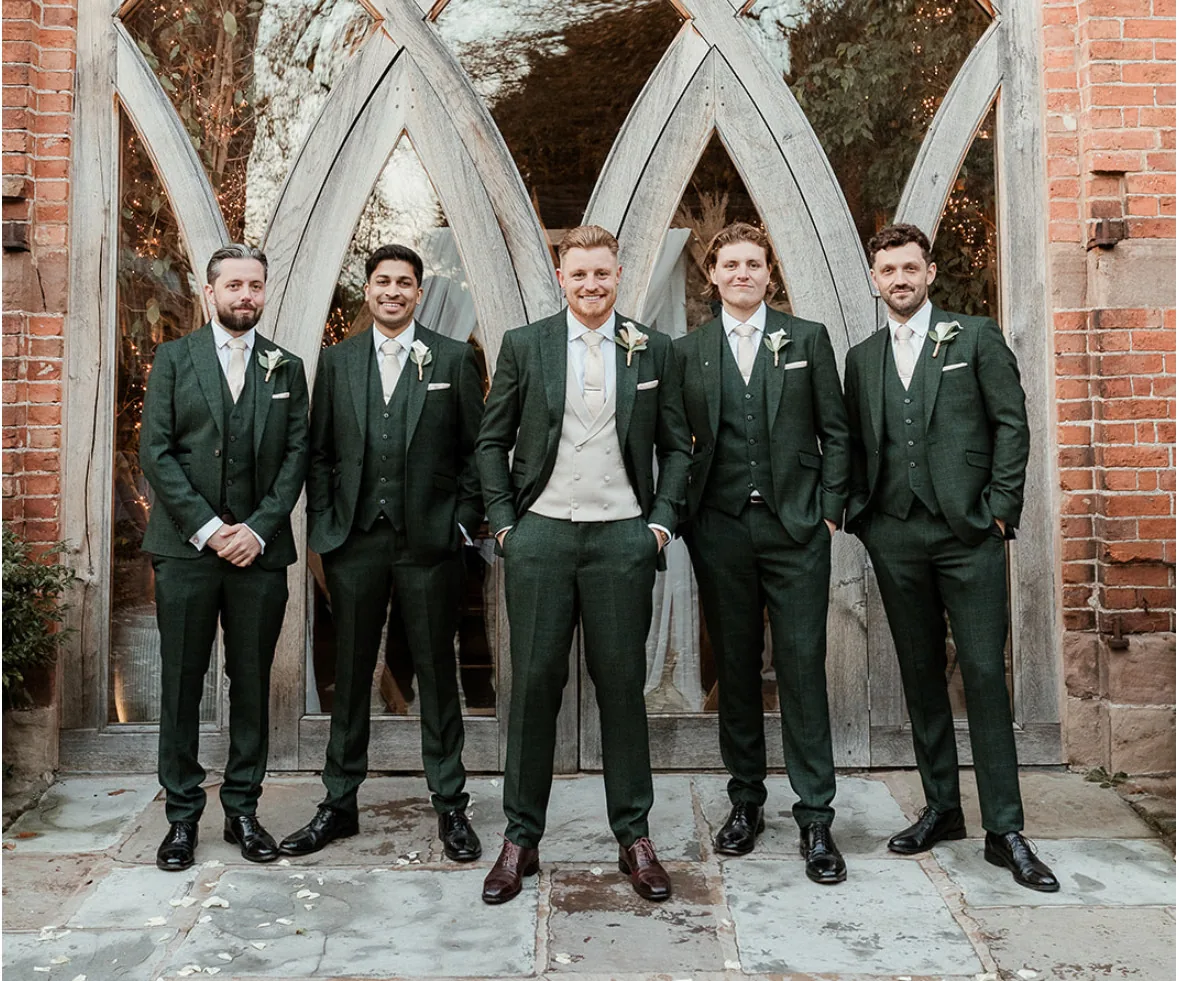 Groom and four groomsmen in green three piece suits outside a wedding venue