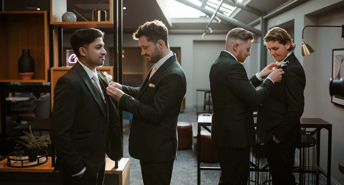 Groom and groomsmen in dark green suits pinning on their buttonholes before the ceremony